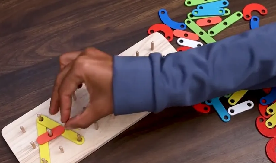 Hand fitting coloured pieces onto the pegs of a wooden pattern board
